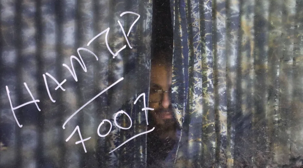 سجين مُفرج عنه من قوات «قسد» ينظر من خلال ستارة حافلة لدى وصوله إلى الحسكة (رويترز)