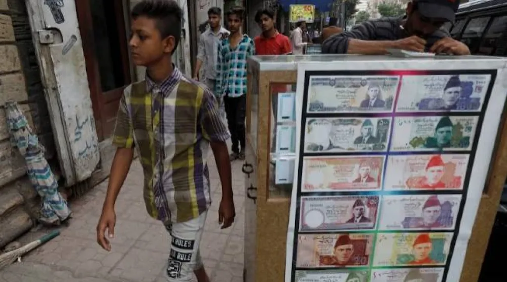 فتى يمر بجوار كشك صرافة مزين بصور الأوراق النقدية في كراتشي (رويترز)