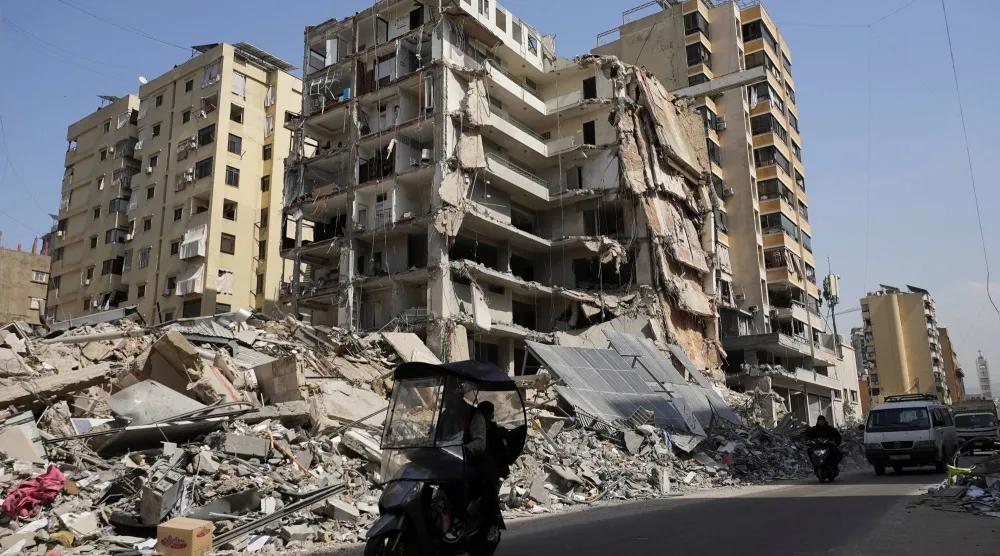 يركب الناس دراجة نارية صغيرة بجوار مبنى متضرر في أعقاب الغارات الإسرائيلية، وسط تصعيد بين حزب الله وإسرائيل (رويترز)