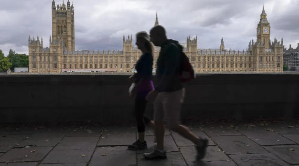 مشاة يسيرون على الضفة الجنوبية لنهر التايمز خلفها قصر وستمنستر في لندن (أ.ف)