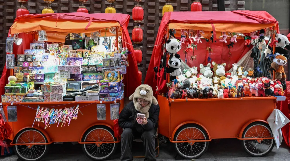 بائعة تتصفح هاتفها بينما تنتظر الزبائن في أحد شوارع العاصمة الصينية بكين (أ.ف.ب)