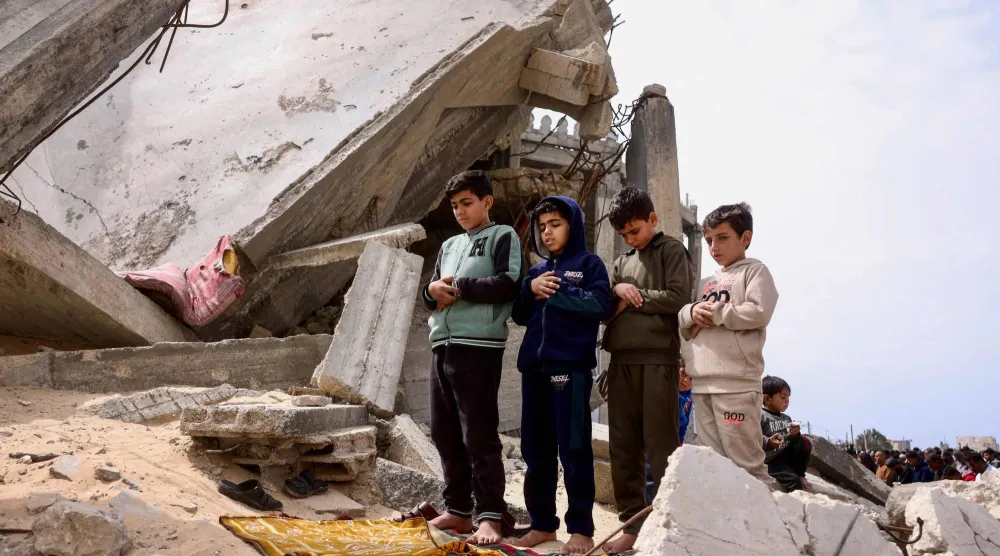 أطفال فلسطينيون يشاركون في صلاة الجمعة فوق أنقاض مسجد الطالباني الذي دمره القصف الإسرائيلي خلال الحرب في خان يونس جنوب قطاع غزة (أ.ف.ب)