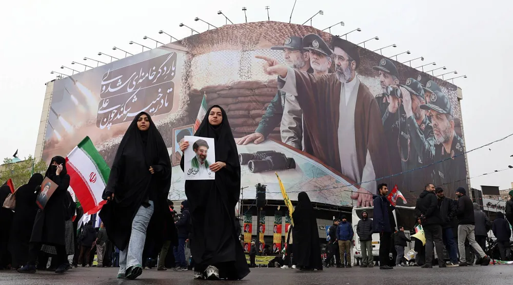 نساء إيرانيات يمشين أمام لوحة تحمل صور المرشد مجتبى خامنئي وقادة عسكريين خلال مسيرة في طهران (إ.ب.أ)