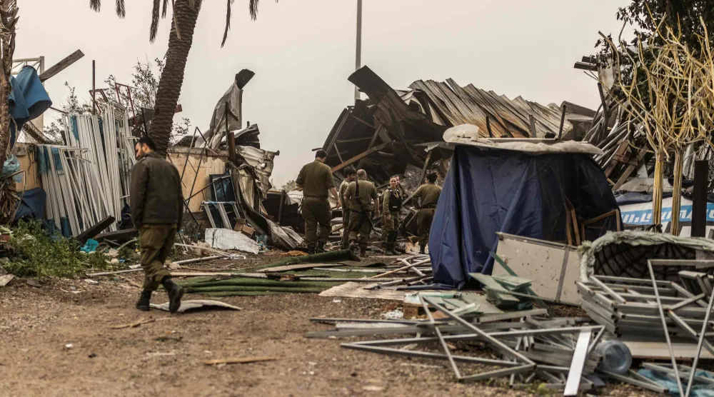 جنود يعاينون أمس الأضرار في مشارف تل أبيب عقب هجوم صاروخي إيراني (أ.ف.ب)