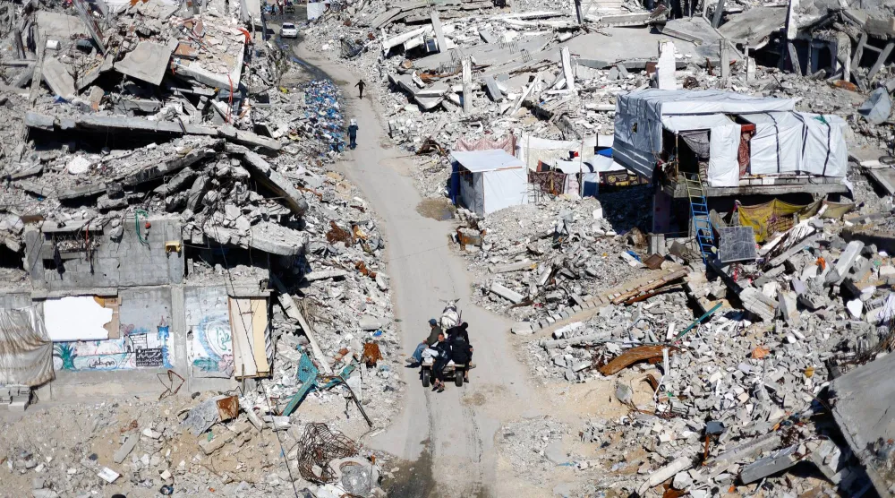 فلسطينيون يمرون أمام أنقاض المباني السكنية التي دُمرتها إسرائيل في جباليا شمال قطاع غزة (رويترز)