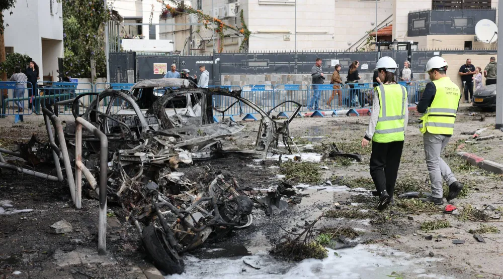 عنصران من خدمة الطوارىء يعاينان سيارات محترقة جراء اعتراض صاروخ باليستي إيراني في تل أبيب أمس (إ.ب.أ)