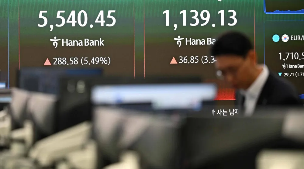 متعامل عملات يراقب أسعار الصرف أمام شاشة تُظهر مؤشري «كوسبي» و«كوسداك» بغرفة تداول ببنك هانا في سيول (أ.ف.ب)