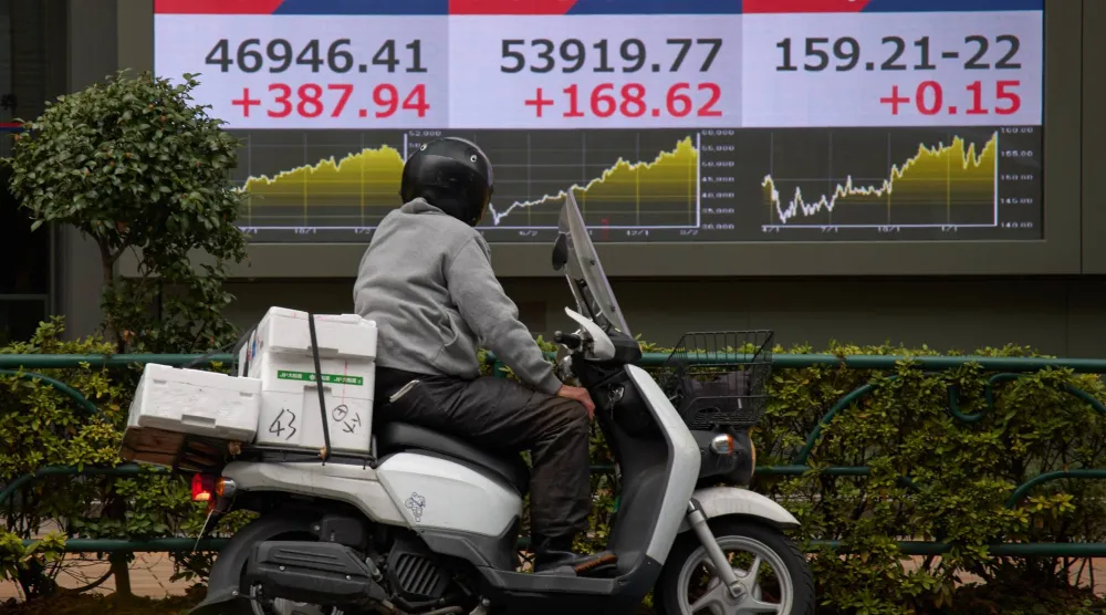 رجل بدراجة نارية أمام لوحة تعرض حركة الأسهم في وسط العاصمة اليابانية طوكيو (أ ب)