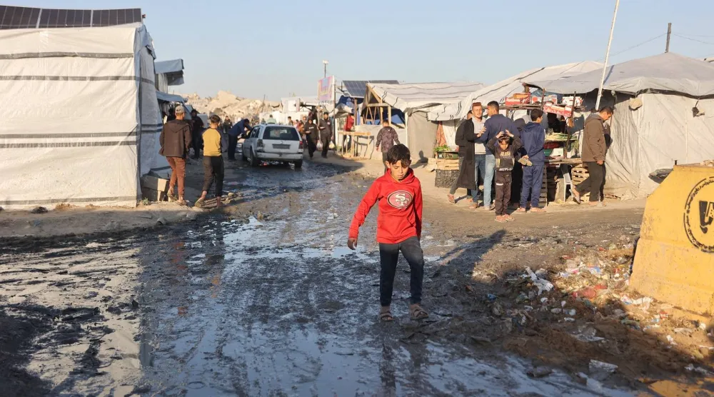 طفل فلسطيني نازح يسير في شارع موحل في مخيم جباليا للاجئين شمال قطاع غزة (أ.ف.ب)