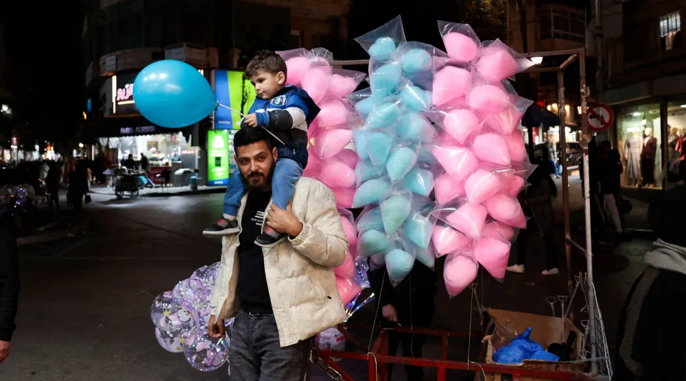 فلسطيني يحمل ابنه يوم الثلاثاء في رام الله بالضفة الغربية قبل حلول عيد الفطر  (رويترز)