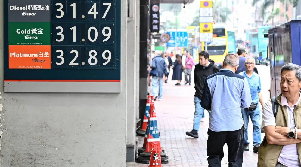 مشاة يمرون أمام لوحة تعرض أسعار الوقود في محطة بمدينة هونغ كونغ الصينية (أ.ف.ب)