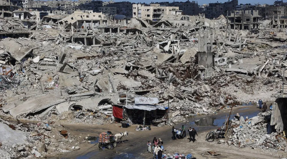 فلسطينيون يشقون طريقهم عبر أنقاض المباني المدمرة في حي الشيخ رضوان بمدينة غزة (أ.ف.ب)