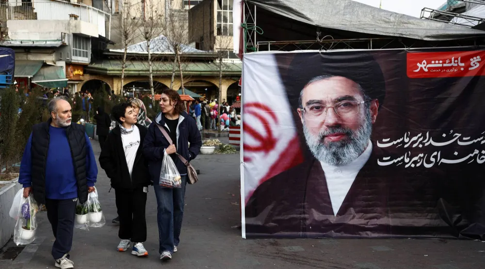 أشخاص يسيرون في طهران بجوار لافتة تحمل صورة المرشد الإيراني الجديد مجتبى خامنئي يوم 19 مارس 2026 (رويترز)