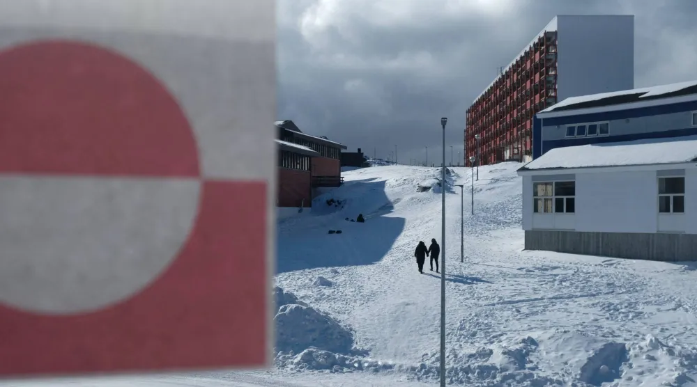 أشخاص يسيرون بجوار علم غرينلاند في نوك (رويترز)