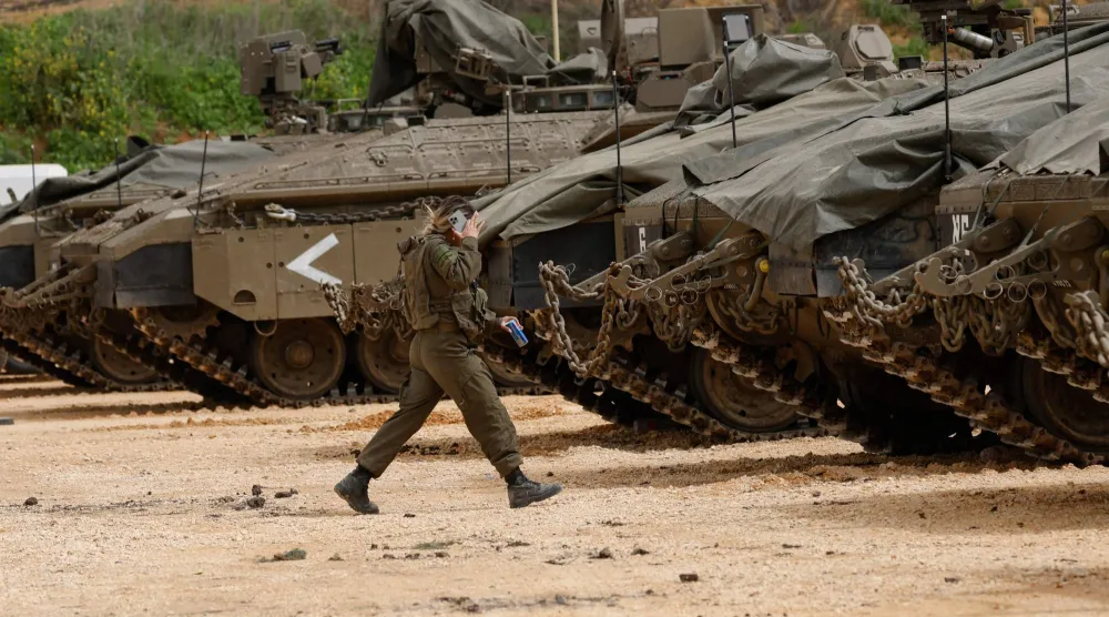 جندية إسرائيلية تسير بين دبابات متجمعة في الجليل الأعلى بالقرب من الحدود الإسرائيلية اللبنانية في 14 مارس 2026 (أ.ف.ب)
