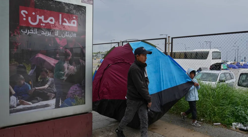 نازح من جنوب لبنان إلى وسط بيروت وإلى جانبه لوحة إعلامية تتضمن شعاراً مناهضاً للحرب (أ.ب)