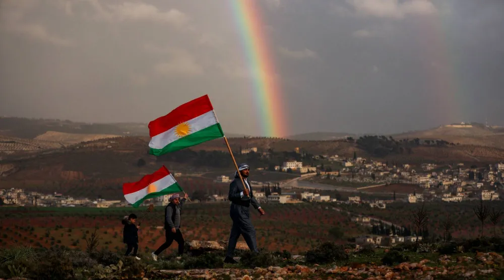 سوريون أكراد يحملون أعلاماً كردية استعداداً للاحتفال بـ«النوروز» في عفرين بمدينة حلب الجمعة (رويترز)