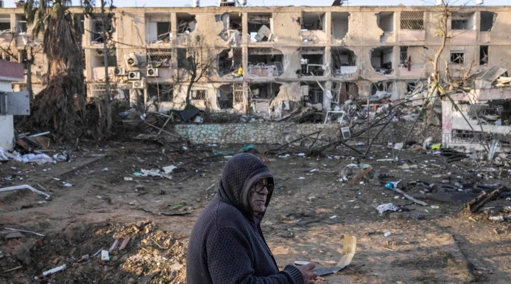 رجل يشرب القهوة بينما ينظر إلى المنازل التي دُمّرت في ضربة صاروخية إيرانية بديمونة (أ.ف.ب)