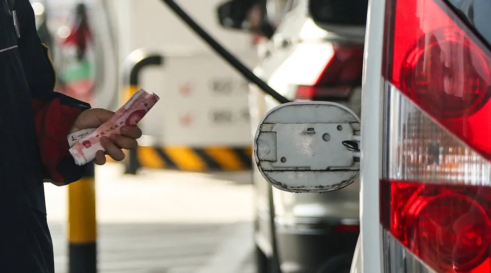 موظف يحمل أوراقاً نقدية من اليوان الصيني بجوار غطاء مفتوح لخزان وقود سيارة في محطة وقود في بكين (رويترز)