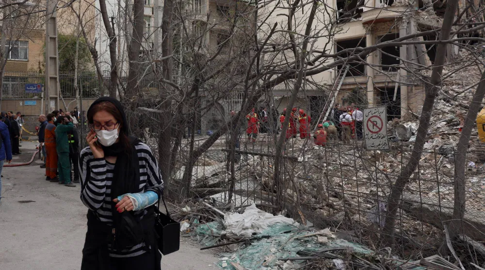 سيدة إيرانية مصابة تسير بجانب مبنى تضرر جراء الغارات الأميركية - الإسرائيلية شمال طهران أمس (إ.ب.أ)