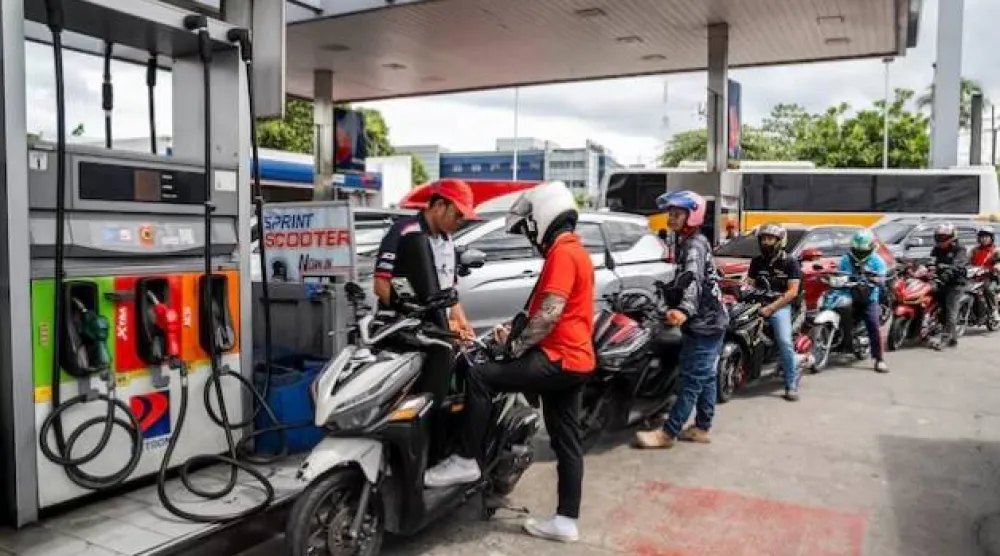 عامل يقوم بتعبئة خزان دراجة نارية بينما يصطف السائقون في محطة وقود بمدينة كويزون- مترو مانيلا (رويترز)