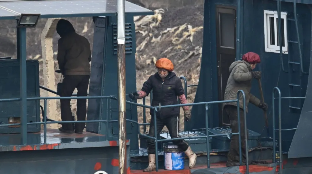 عمال كوريون شماليون يطلون قارباً على ضفة نهر يالو في بلدة سينويجو الكورية الشمالية (أ.ف.ب)