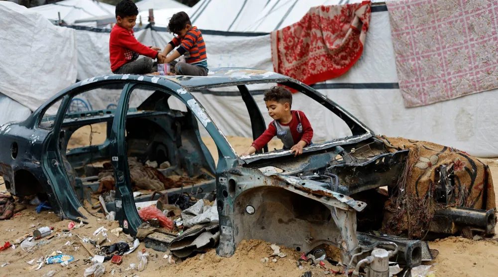 أطفال فلسطينيون نازحون يلعبون على حطام سيارة في مخيم بالنصيرات وسط غزة يوم الأربعاء (رويترز)