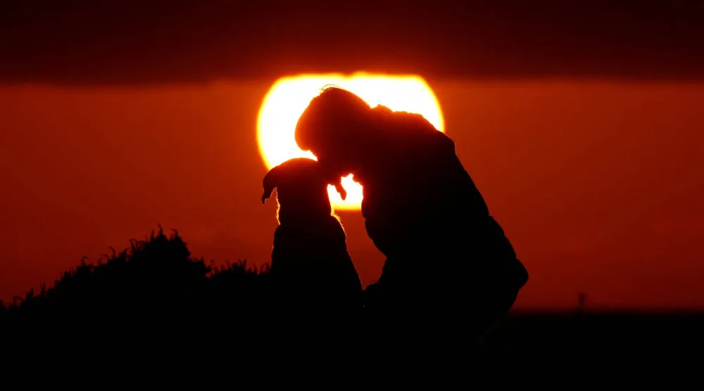 امرأة تُقبّل كلبها أثناء مشاهدتهما غروب الشمس في مالطا (رويترز)