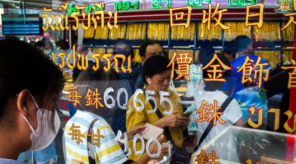 أحد الموظفين يقوم بتحديث أسعار الذهب بينما يصطف الزبائن داخل متجر للذهب في الحي الصيني ببانكوك (أ.ف.ب)