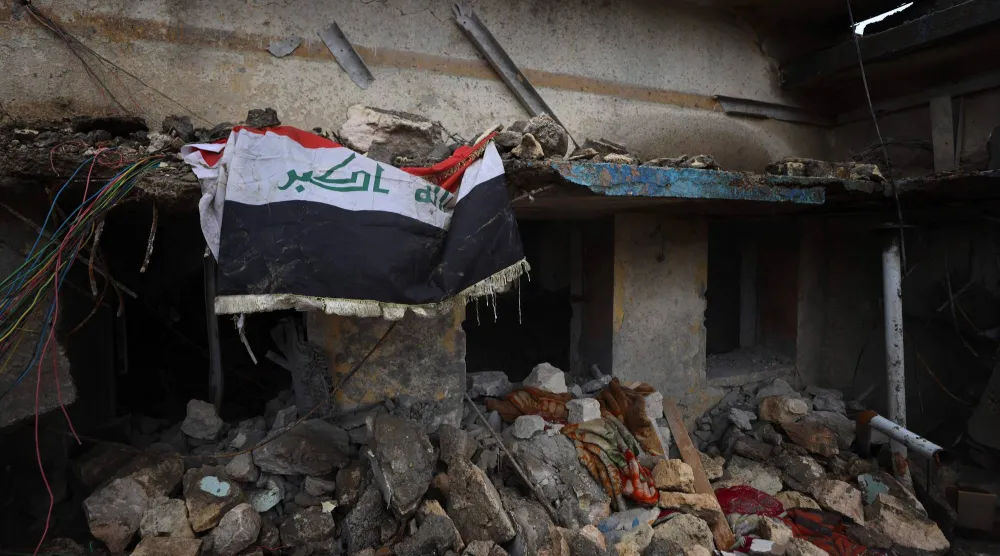 علم العراق معلقًا فوق الأنقاض في موقع مُدمَّر داخل قاعدة الحبانية العسكرية غرب البلاد (أ.ف.ب)