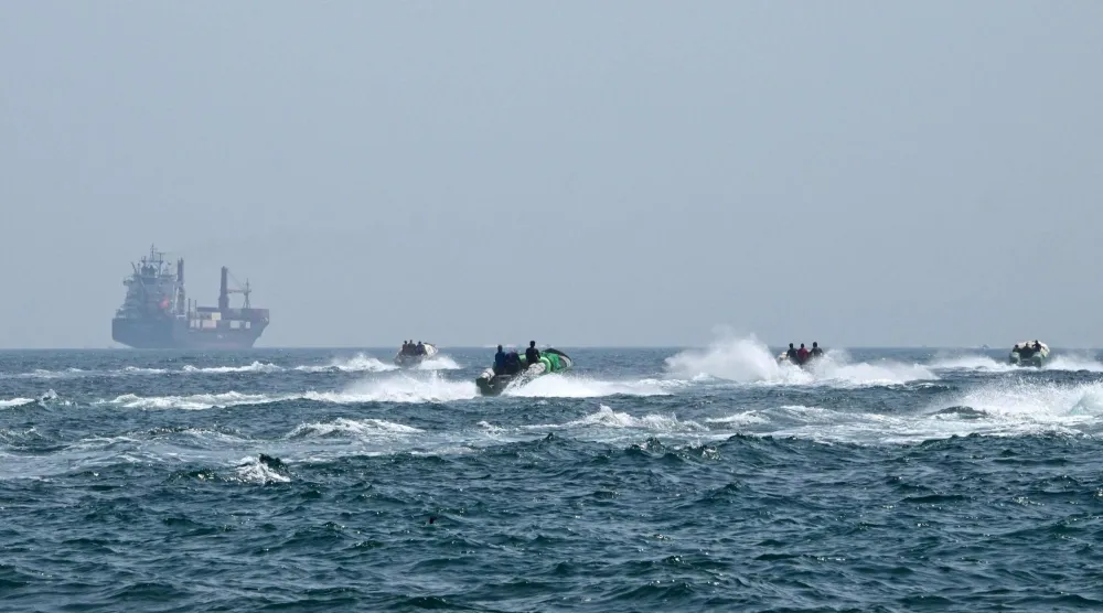 قوارب صغيرة تبحر محملة بالبضائع أمام سفينة حاويات في مياه مضيق هرمز قبالة سلطنة عمان 25 يونيو 2025 (أ.ف.ب)