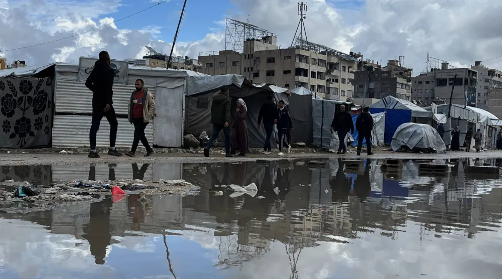 نازحون فلسطينيون يمشون إلى جانب خيامهم التي غمرتها مياه الأمطار في مدينة غزة يوم الخميس (د.ب.أ)