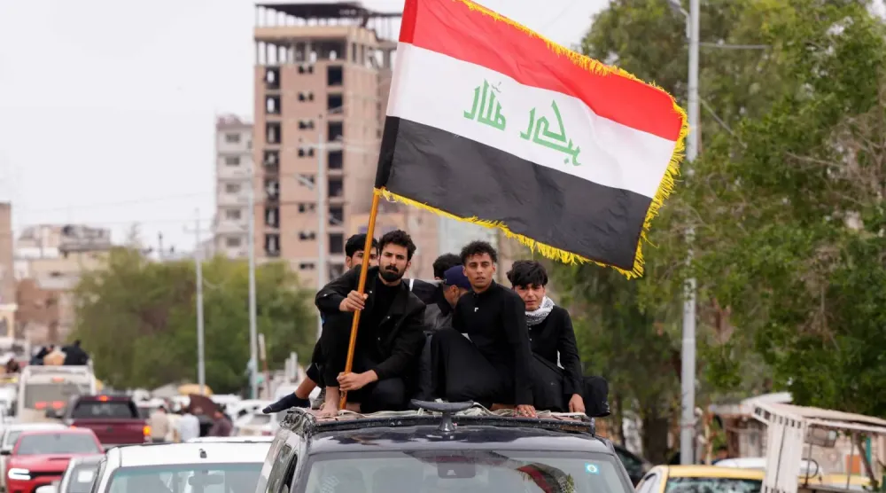 Habbaniye üssüne düzenlenen hava saldırısında hayatını kaybeden askerin yakınları, cenaze töreni sırasında Irak bayrağını dalgalandırıyor (AFP)