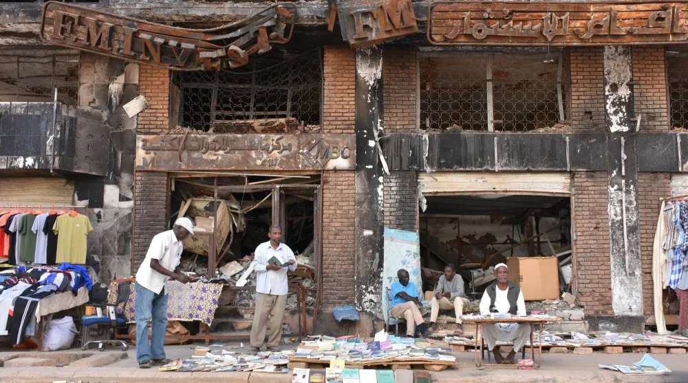 يبيع الناس بضائعهم أمام مبنى متضرر في الخرطوم (د.ب.أ)