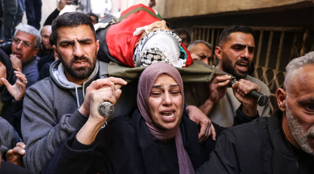 والدة الفتى آدم دهمان (15 عاماً) الذي قتله الجيش الإسرائيلي تحمل جثمانه خلال جنازته في مخيم الدهيشة ببيت لحم في الضفة الغربية المحتلة (أ.ف.ب)