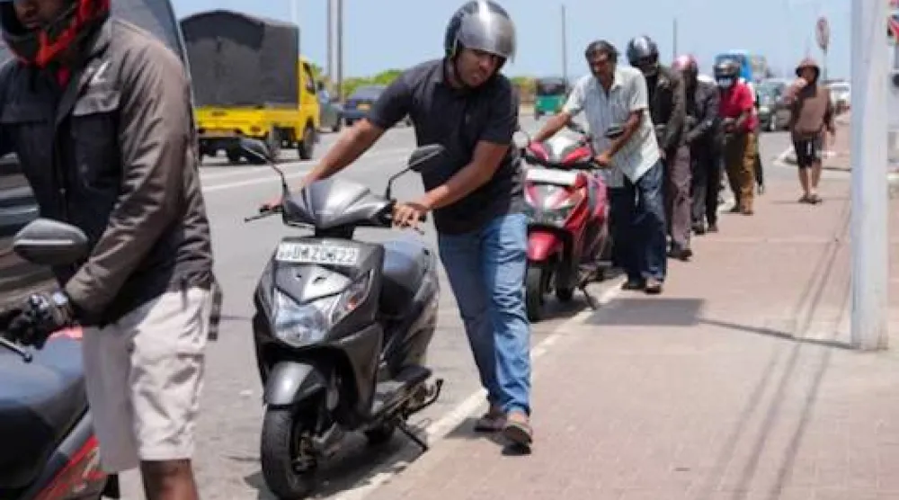 أشخاص يقفون في طابور أثناء انتظارهم لتزويد دراجاتهم النارية بالوقود في كولومبو (رويترز)