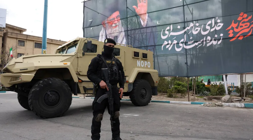 أحد أفراد قوات الأمن الإيرانية يقف حارساً بجوار لافتة للزعيم الإيراني السابق علي خامنئي في طهران 30 مارس 2026 (إ.ب.أ)