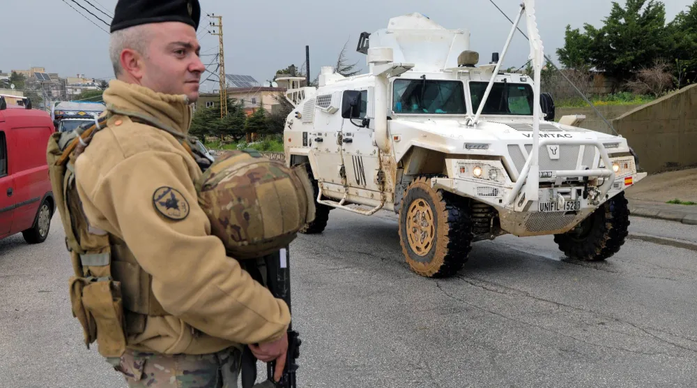 مركبة تابعة لقوات «يونيفيل» تمر بجانب جندي لبناني وسط تصاعد الأعمال العدائية بين إسرائيل و«حزب الله» (رويترز)