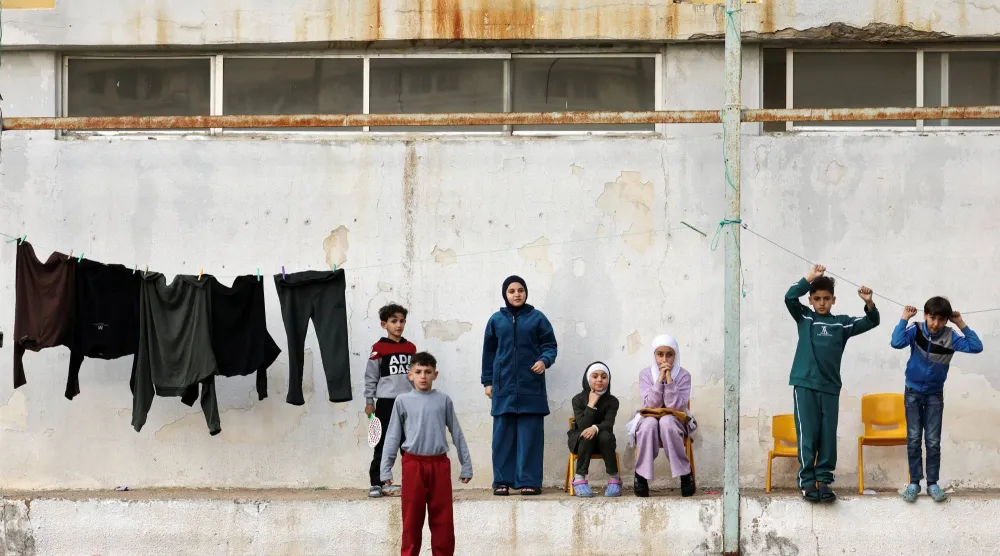 مجموعة من الأطفال النازحين يتجمعون داخل حرم مدرسة ثانوية تُستخدم الآن مأوى مؤقتاً وسط الضربات الإسرائيلية على لبنان (رويترز)