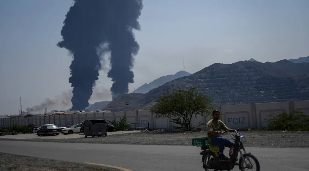 رجل يقود دراجة هوائية بينما تتصاعد النيران وأعمدة الدخان بعد أن أصاب حطام طائرة إيرانية مُسيَّرة تم اعتراضها منشأة نفطية وفقاً للسلطات في الفجيرة يوم 14 مارس الحالي (أ.ب)