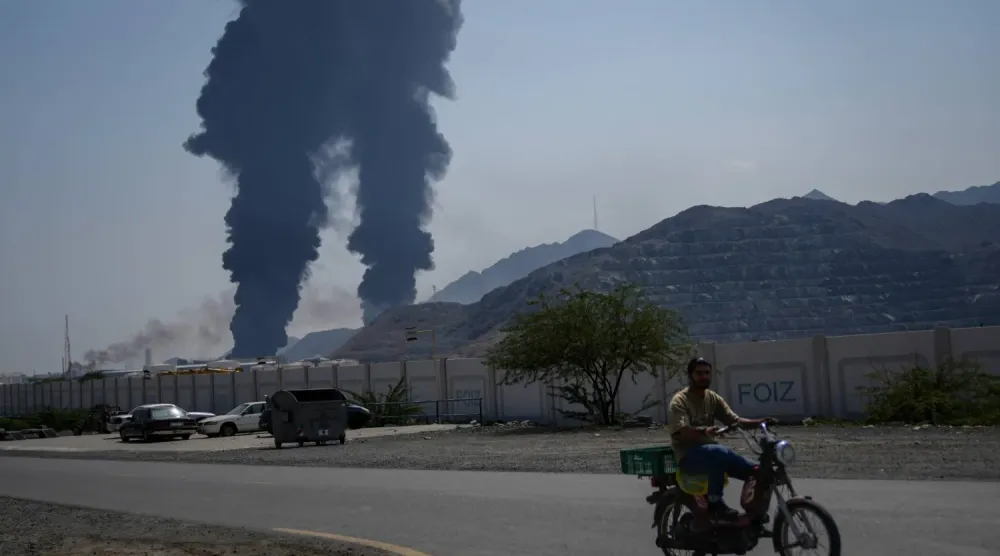  Fuceyre'deki yetkililere göre 14 Mart'ta İran'a ait İHA enkazının bir petrol tesisine isabet etmesinin ardından yükselen alevler ve duman bulutları arasında bir adam bisiklet sürüyor (AP)