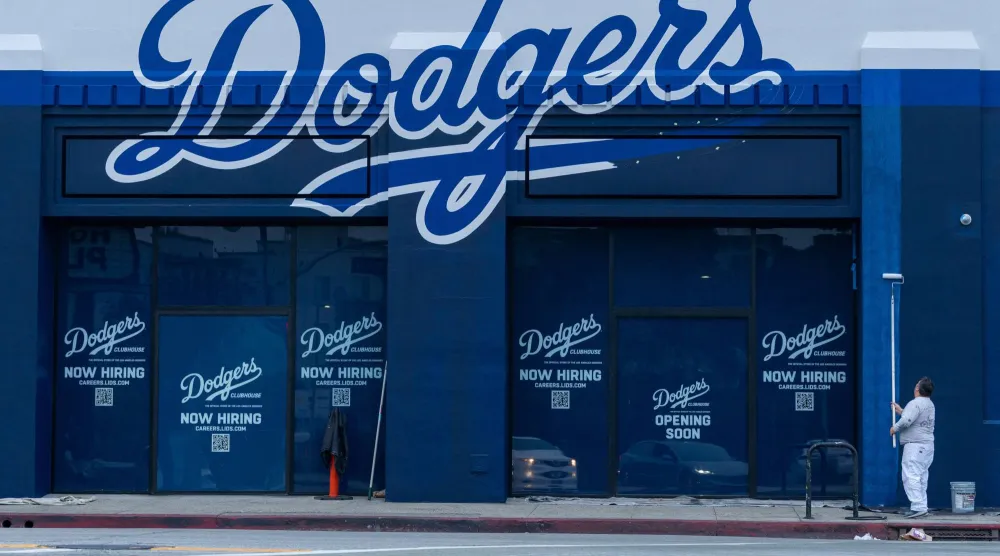 عامل يدهن الجدران الخارجية لمبنى يعرض وظائف لدى فريق «لوس أنجليس دودجرز» وسط مدينة لوس أنجليس (رويترز)