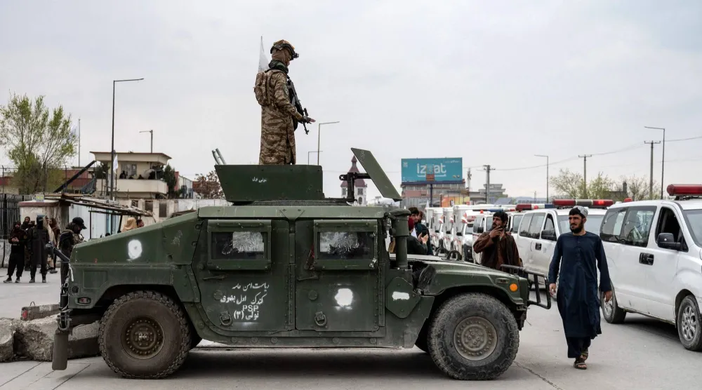 عنصر من «طالبان» يقف فوق مركبة مدرعة بينما تنقل سيارات الإسعاف توابيت ضحايا غارة جوية باكستانية في كابل (أ.ف.ب)