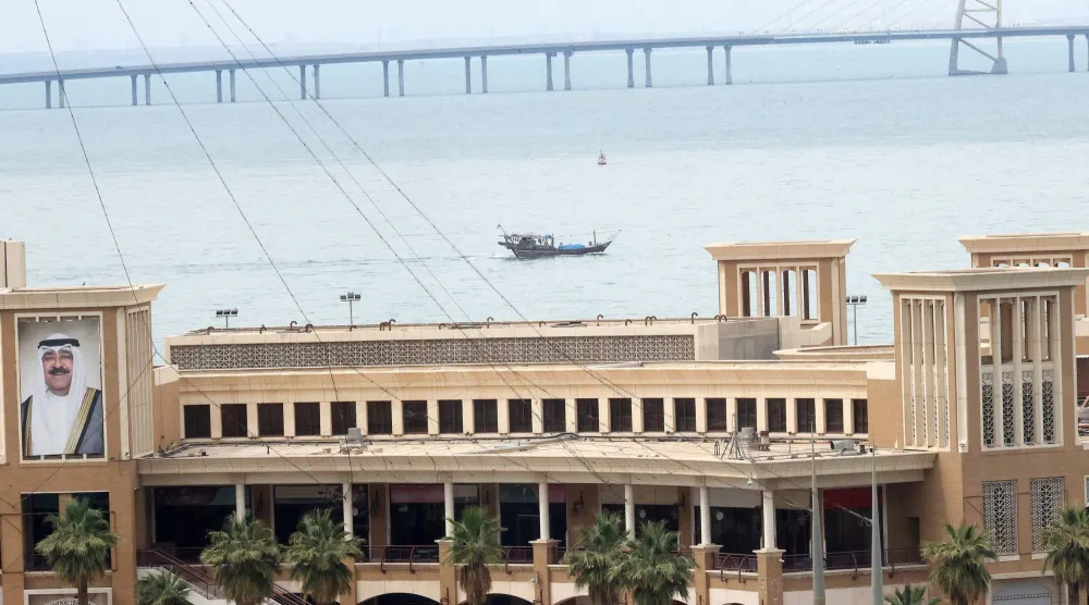 قارب صيد يبحر في مياه الخليج العربي بمدينة الكويت، ويظهر جسر الشيخ جابر الأحمد الصباح في الخلفية (أ.ف.ب)