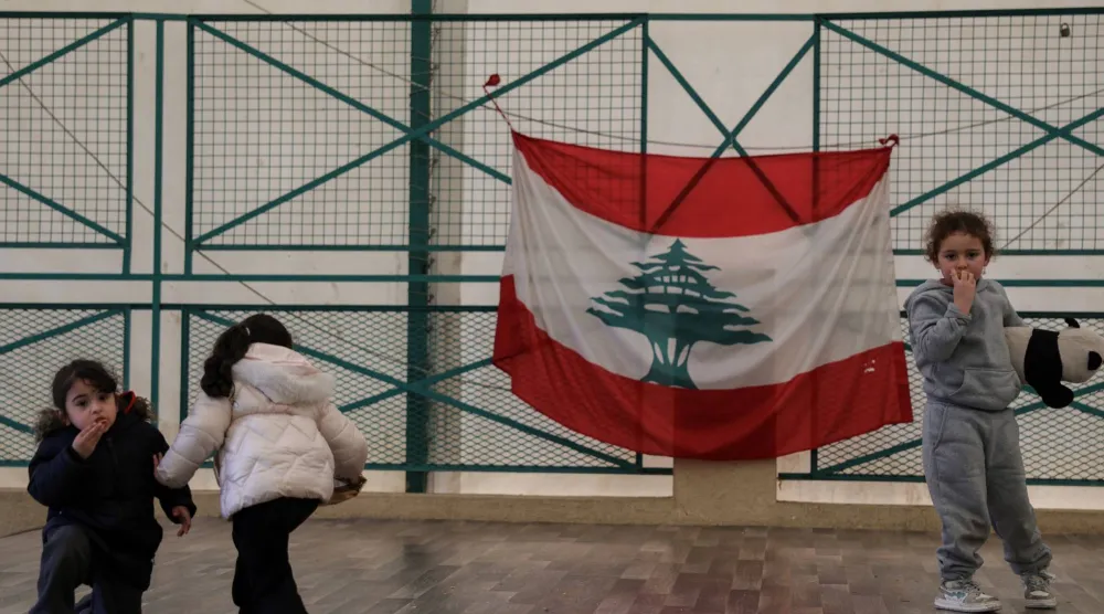 أطفال نازحون يلعبون في مدرسة تحولت إلى مركز للنزوح ومن خلفهم العلم اللبناني (رويترز)