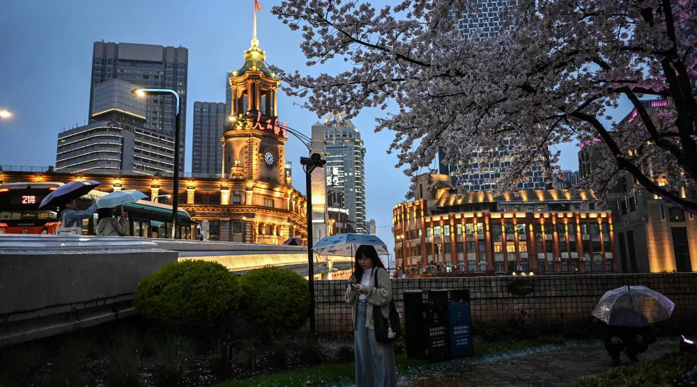 سيدة تسير تحت الأمطار في مدينة شنغهاي الصينية (أ.ف.ب)