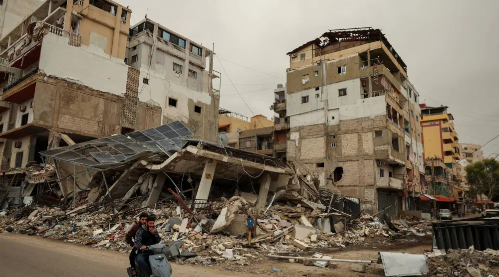 رجلان على دراجة نارية يمران أمام أنقاض مبنى دمّرته غارة إسرائيلية (رويترز)