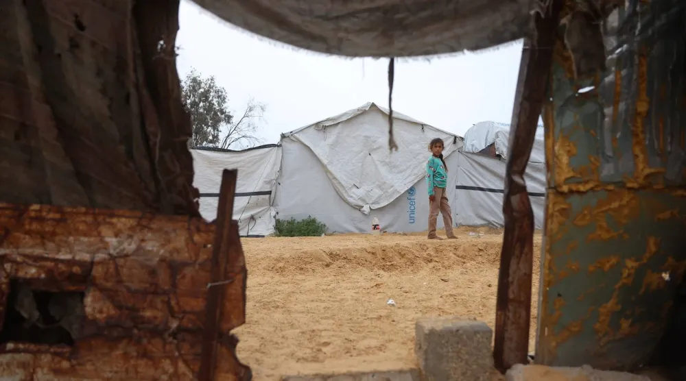 فتاة تقف بجوار خيمة في مخيم مؤقت للنازحين الفلسطينيين في منطقة نهر البارد في خان يونس جنوب قطاع غزة (أ.ف.ب)