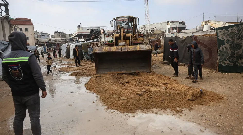 جرافة تقوم بإزالة المياه من شارع غمرته المياه في مخيم مؤقت يؤوي نازحين فلسطينيين في خان يونس (أ.ف.ب)