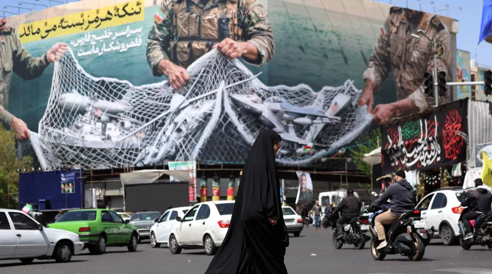 ركابٌ يمرّون أمام لوحة إعلانية كُتب عليها «مضيق هرمز لا يزال مغلقاً» في ساحة انقلاب بطهران (أ.ف.ب)